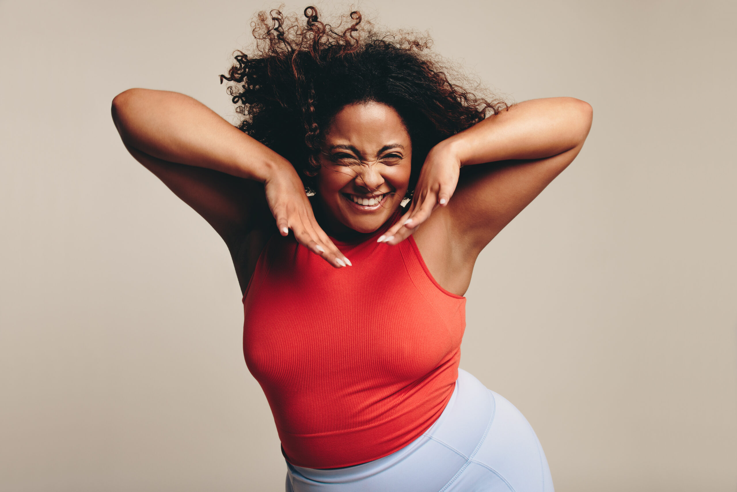 Excited woman with a fit and curvy form having a great time in a lively and expressive dance workout. She celebrates her body, proudly showing her confidence and self-assurance as she expresses herself through body movement.